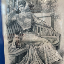 Magazine card: Elegant lady in a summer dress sitting on a bench. Next to her is a small dog.
