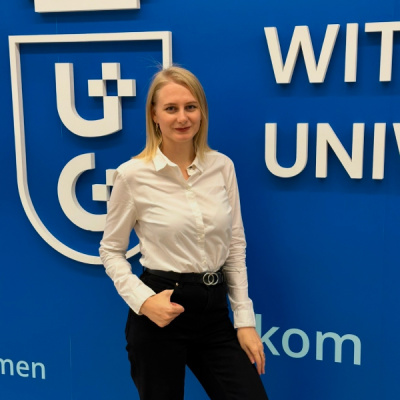Dr Halyna Alekseievska at navy wall with white logotype of Uniwersity of Gdańsk