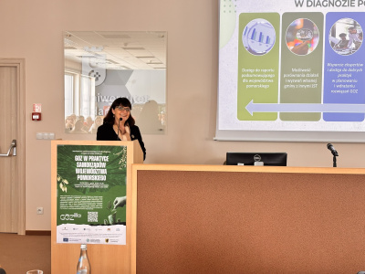 Dr Magdalena Markiewicz przy mównicy, w tle za nią fragment prezentacji
