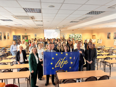 Uczestnicy seminarium w sali seminaryjnej, z przodu trzymają flagę - na fladze UE napis LIFE wewnątrz okręgu z Gwiazd