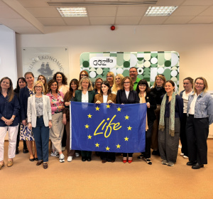 Zdjęcie grupowe uczestników seminarium; stoją na tle planszy z nazwą projektu, przed sobą trzymają flagę opartą na fladze UE z napisem LIFE w środku okręgu z gwiazd