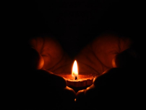 Na zdjęciu świeczka trzymana w dłoniach, której płomień rozświetla ciemność