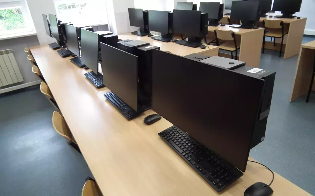widok w jednej z przykładowych pracowni komputerowych pokazujący układ stanowisk komputerowych - biurka, krzesła, zestawy komputerowe