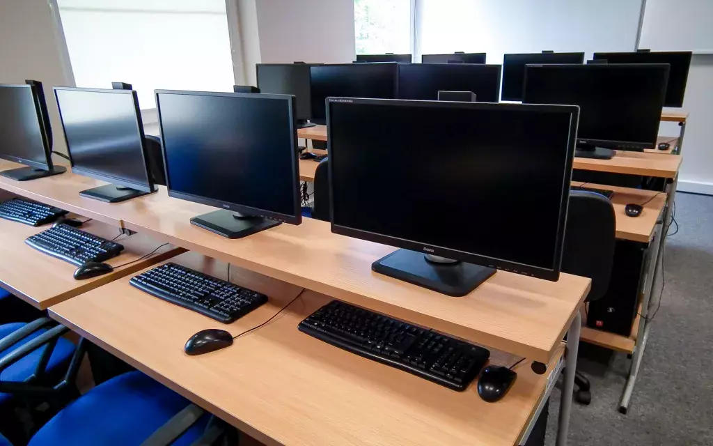 widok jednej z przykładowych pracowni komputerowych wyraźnie widać ustawienie krzeseł, ławek szkolnych oraz zbliżenie na zestawy komputerowe