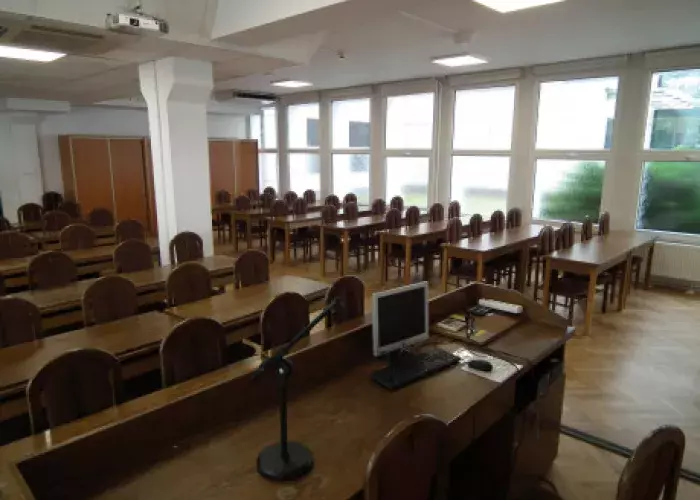 widok sali konferencyjnej od strony podestu . wyraźnie widoczne drewniane meble, stół dla prowadzącego z przykładowym wyposażeniem multimedialnym : komputer stacjonarny, mikrofon