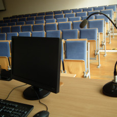 widok auli od przodu od strony podestu, na pierwszym planie widoczne biurko prowadządcego z przykładowym wyposażeniem multimedialnym : komputer stacjonarny, mikrofon